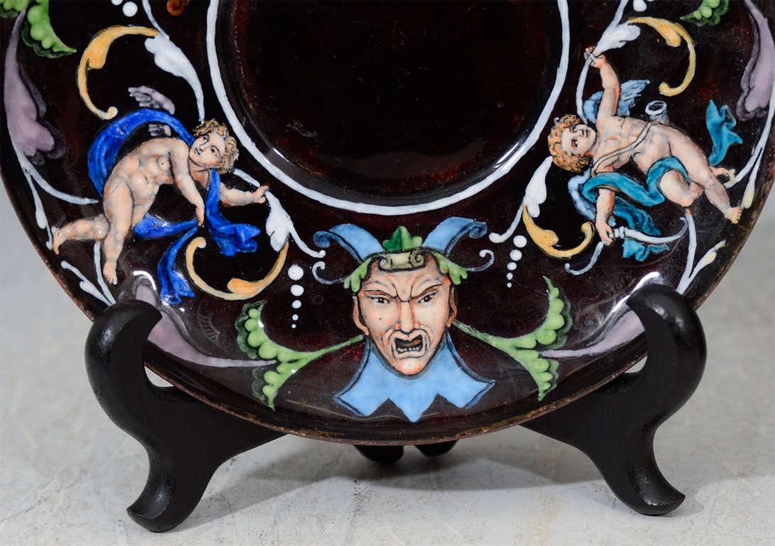 A single Limoges cup and saucer. Each is decorated with a colorful 16th century motif in vitreous enamel over metal depicting cherubs, animals and jesters.