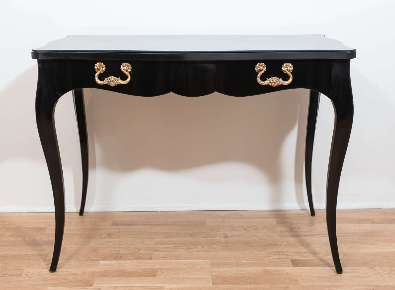 A gorgeous and elegant French Regency style writing table or vanity  with ebonized base and a new black glass top. This sumptuous desk has beautifully proportioned cabriolet legs and two drawers with exquisite weighty ormolu handles.