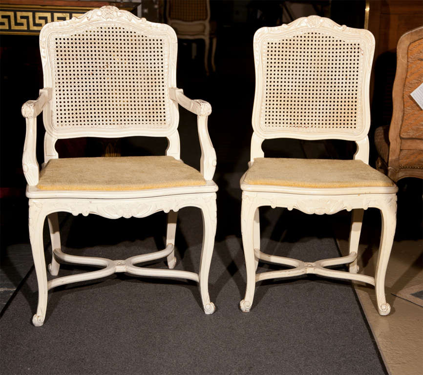 Set of six French dining chairs, circa 1950s, in the taste of French Louis XV, each white painted and distressed finish, the set consists of two armchairs and four side chairs, caned back and padded seat, raised on cabriole legs with X stretchers.