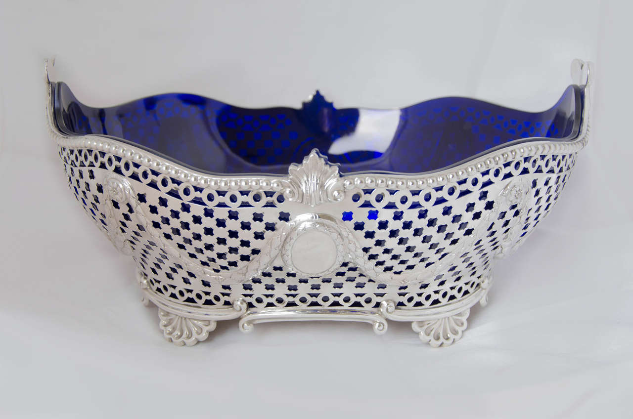 An large antique Victorian sterling silver jardiniere with blue glass liner. The shaped dish is pierced all-over; has a beaded border; and stands on four shell feet.