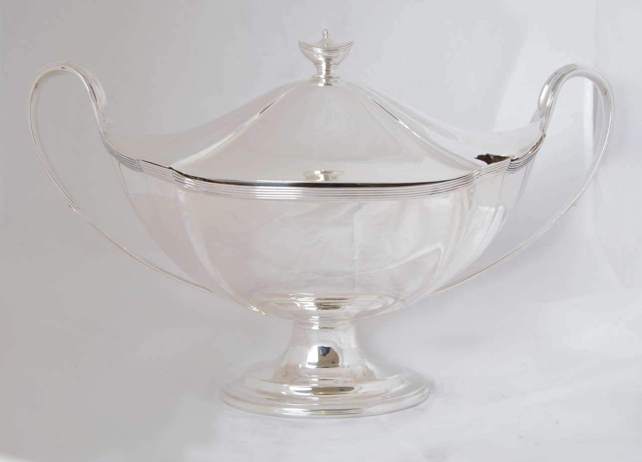 An antique Victorian silver soup tureen and cover of shaped oval form and having a reeded border. 
The height to the top of the urn-shaped finial is 9.5"; it is 14.75" across the handles; and the width is 7.75".
This soup tureen has a