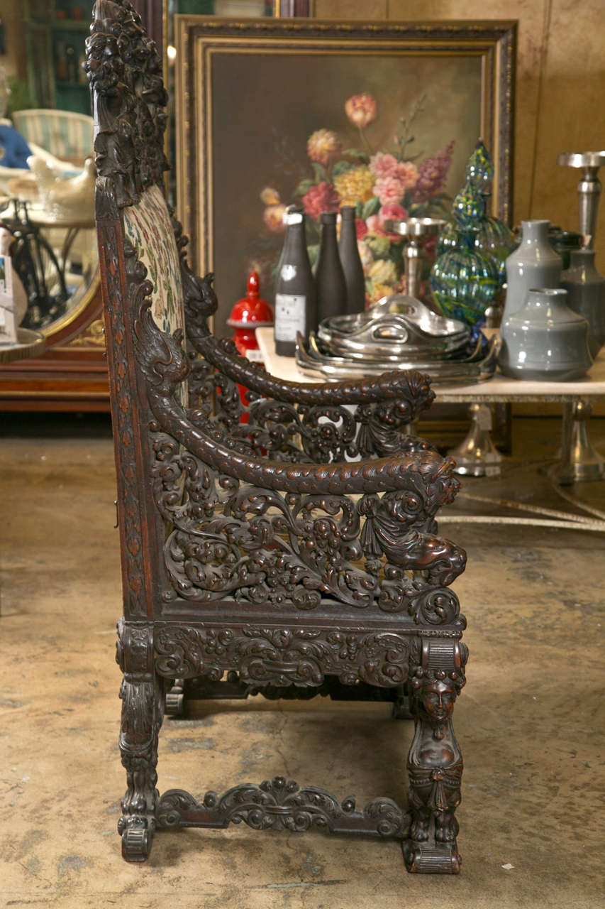 All original, antique, over sized hand carved mahogany throne chair.  It is garnished with bows and wreaths.  Depicts faces of gods and angels.  It is palatial for sure. The seat under the cushion is intricately carved as well. The ends of the arms