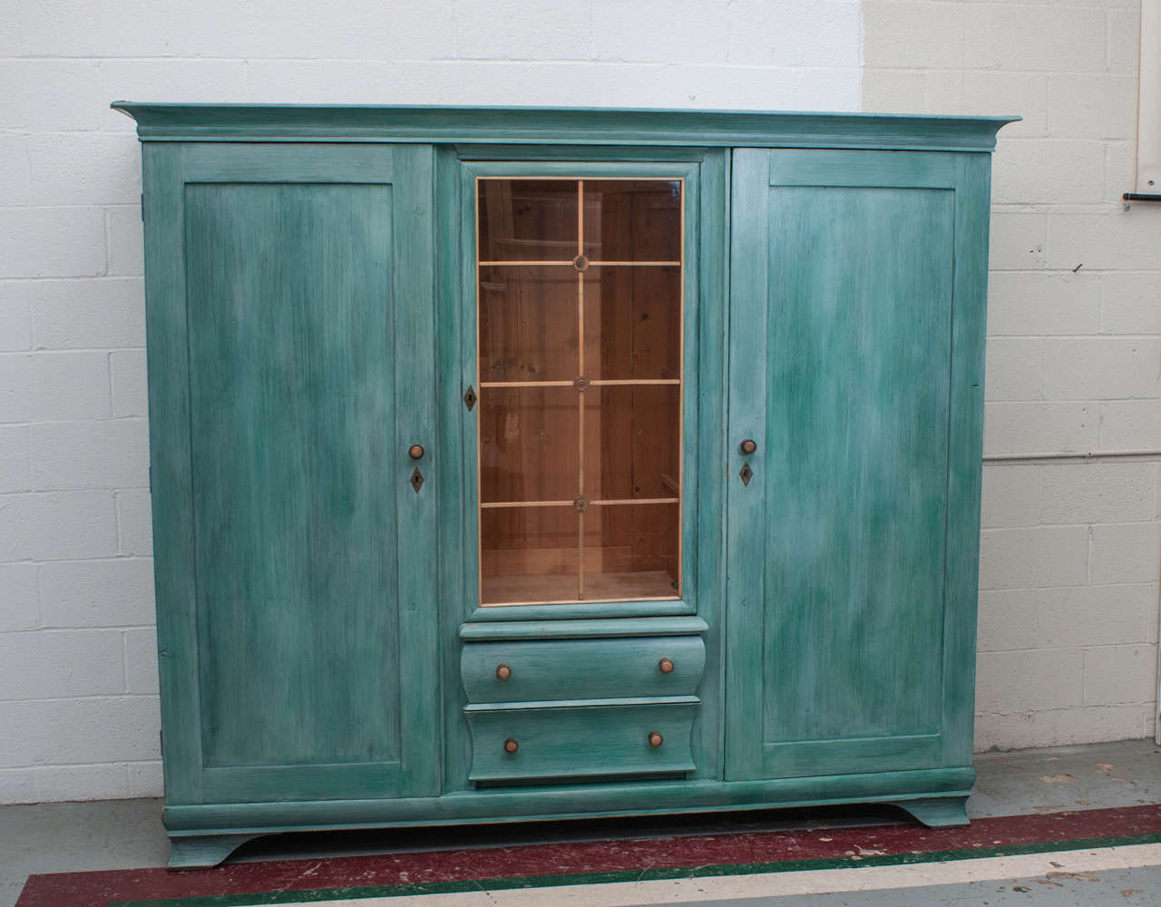 This large and unusual triple armoire offers heaps of storage.  It features a central glazed door above one convex and one concave fronted drawer, flanked by wide swinging doors revealing two wide and deep compartments for shelves or hanging poles. 