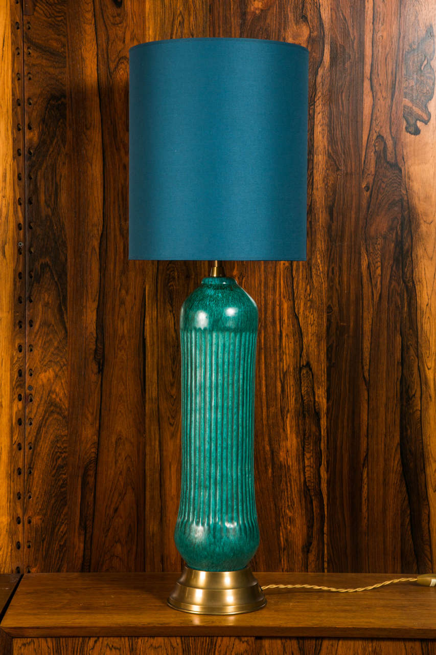 Tall stoneware with incised decor on the front and beautifull green/blue glaze color, orginal brass round base.
The shade is newly done with gold color inside.
Unique piece created by the ceramist Marcello Fantoni during the 1950s.