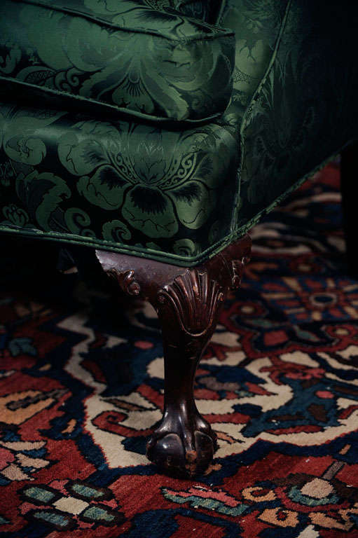 In George III taste, the serpentine backrest flanked by outscrolled arms, raised on cabriole legs carved with shells and acanthus at the knees and ending in ball and claw feet.