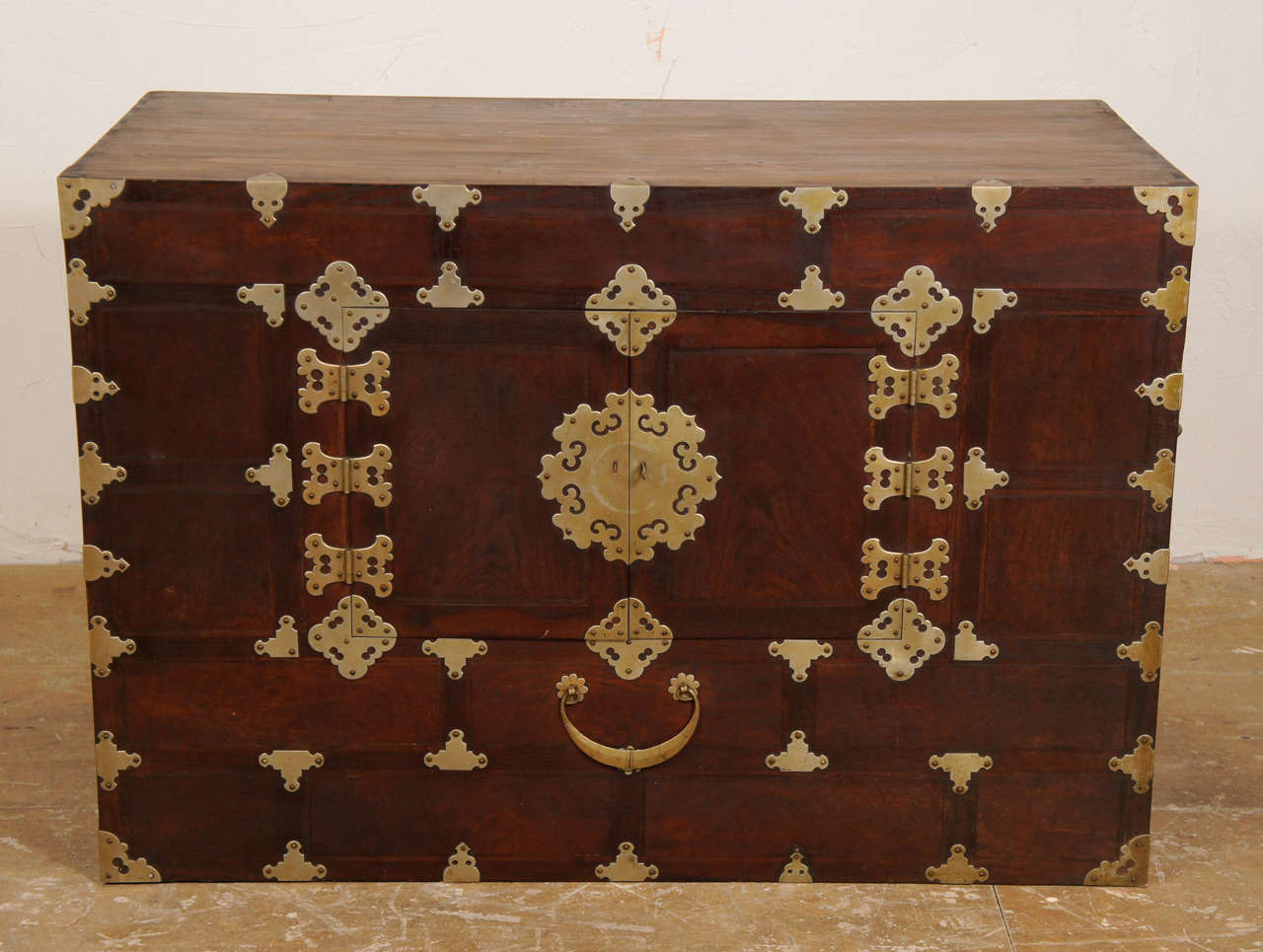 Elegant Chinese chest with decorative brass hinges, handle and iron carrying handles.  Lightweight wood/partially tongue and groove.  Small double center doors (partly missing latch) lead to one large interior lined in paper -- no shelves -- great