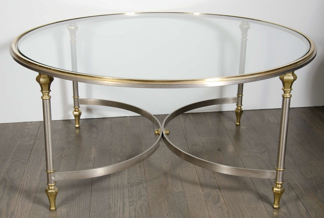 Gorgeous round silvered and brass cocktail table with a glass inset top. Stylized balustrade design legs with opposing arc supports.