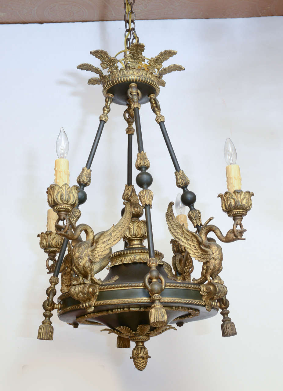 Period Empire chandelier, originally oil burning, of patinated and gilt bronze; having a round centre with ormolu embellishments, suspended by a matching crown and trio of decorative bars, four electrified candles finish arms fashioned as winged