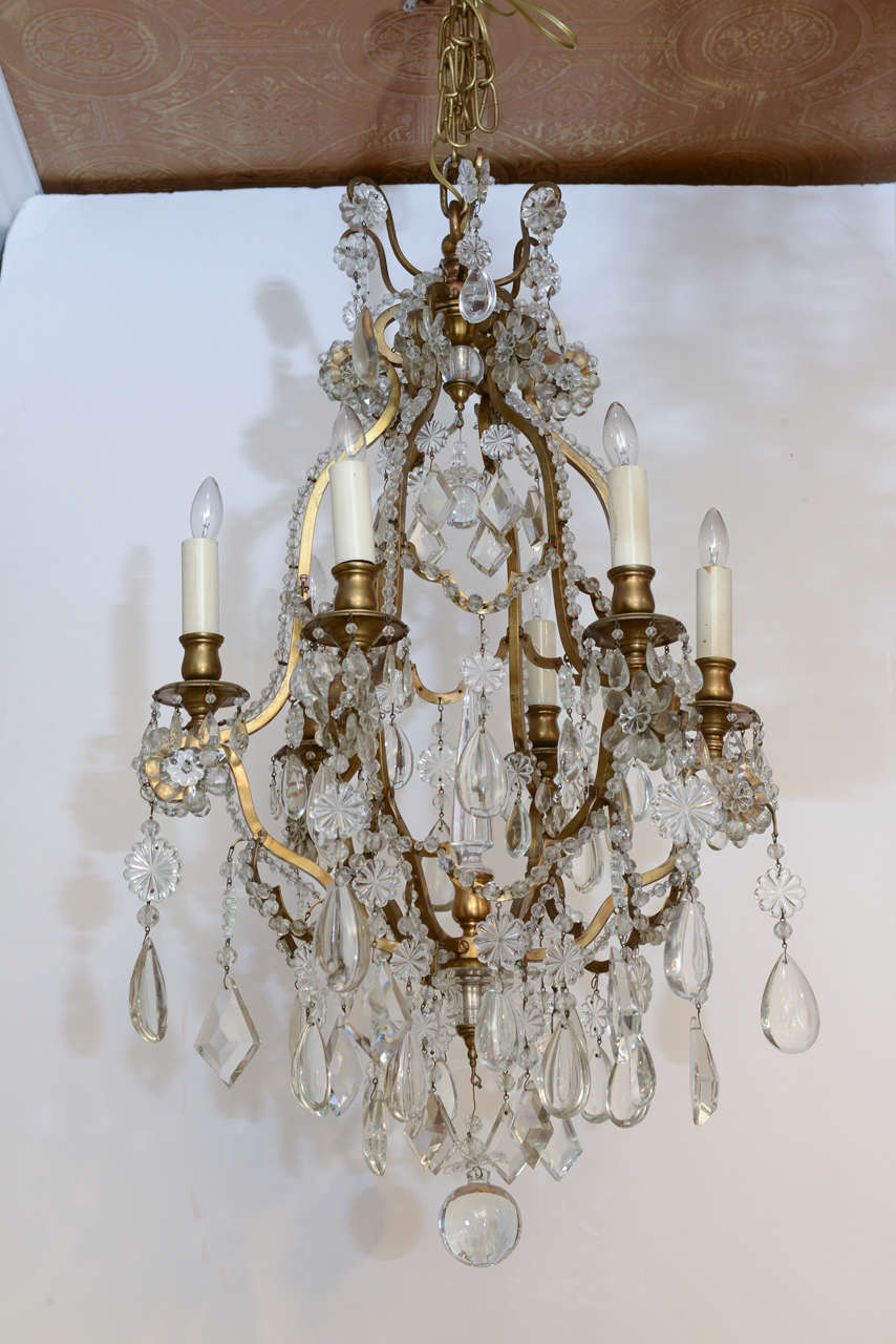 Very fine chandelier, having an open-cage form of gilt brass with six lights, each candle arm decorated with crystal flowers (image 5), its serpentine frame lined with beads, surrounding a central cut crystal spire, surmounted by a gallery of