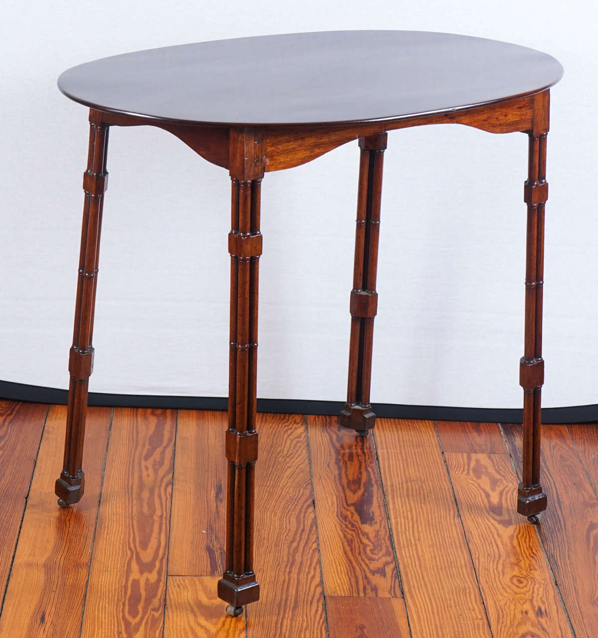 Solid mahogany oval topped Regency table with curved skirt and bamboo carved legs on casters.