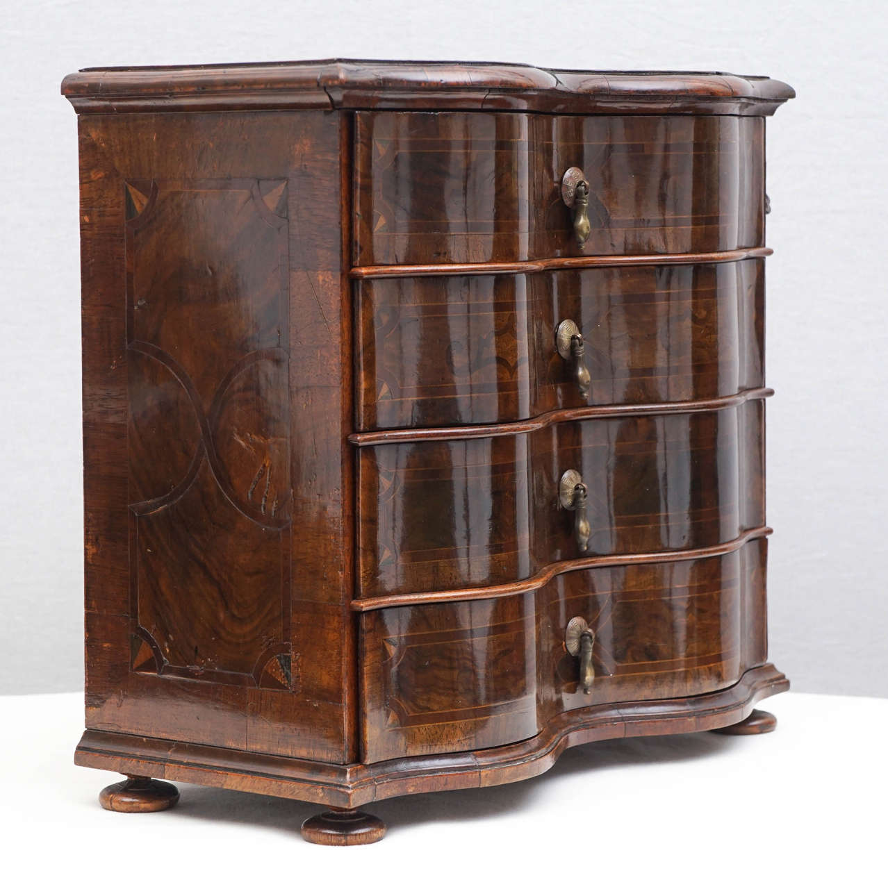 German Rococo-style walnut inlaid miniature serpentine-fronted chest of drawers, with locking device and key. Teardrop metal drawer pulls. Intricate
locking device that secures all the drawers. Interior of all the drawers painted
in precious metal