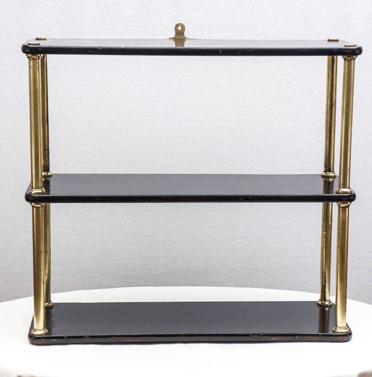 Ebonized wood and brass three-tier hanging shelf.