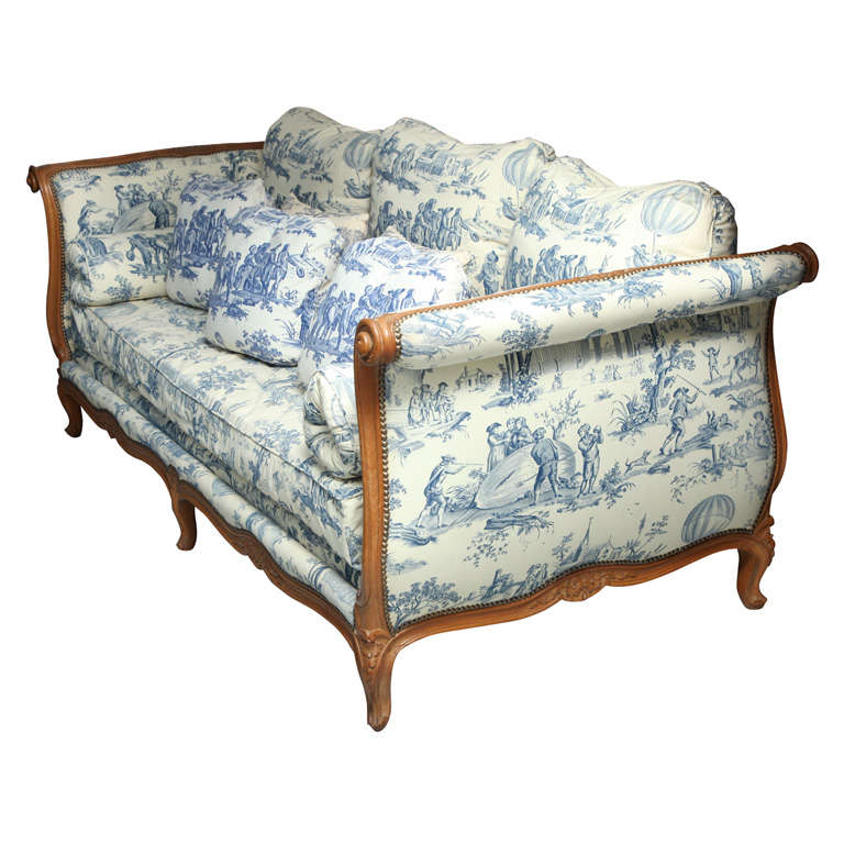 A French Louise XVI style hand carved fruitwood daybed with bolster cushions and back pillows upholstered in blue and white “Montgolfier” print Toile de Jouy.