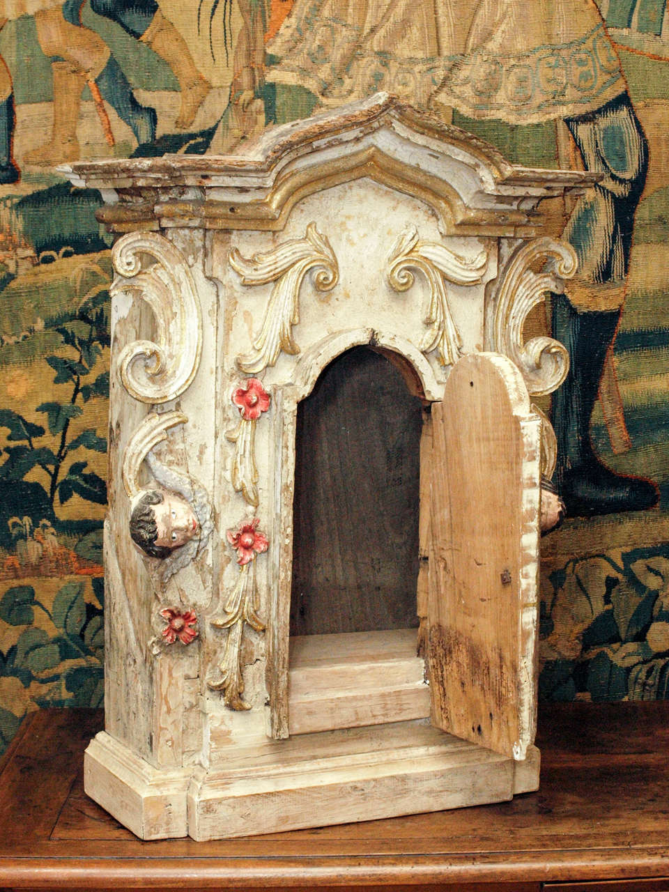An exuberantly and finely carved tabernacle or altar cabinet, the cabinet with a single, arched door mounted by a deeply molded and arched cornice, the sides mounted by putti. 