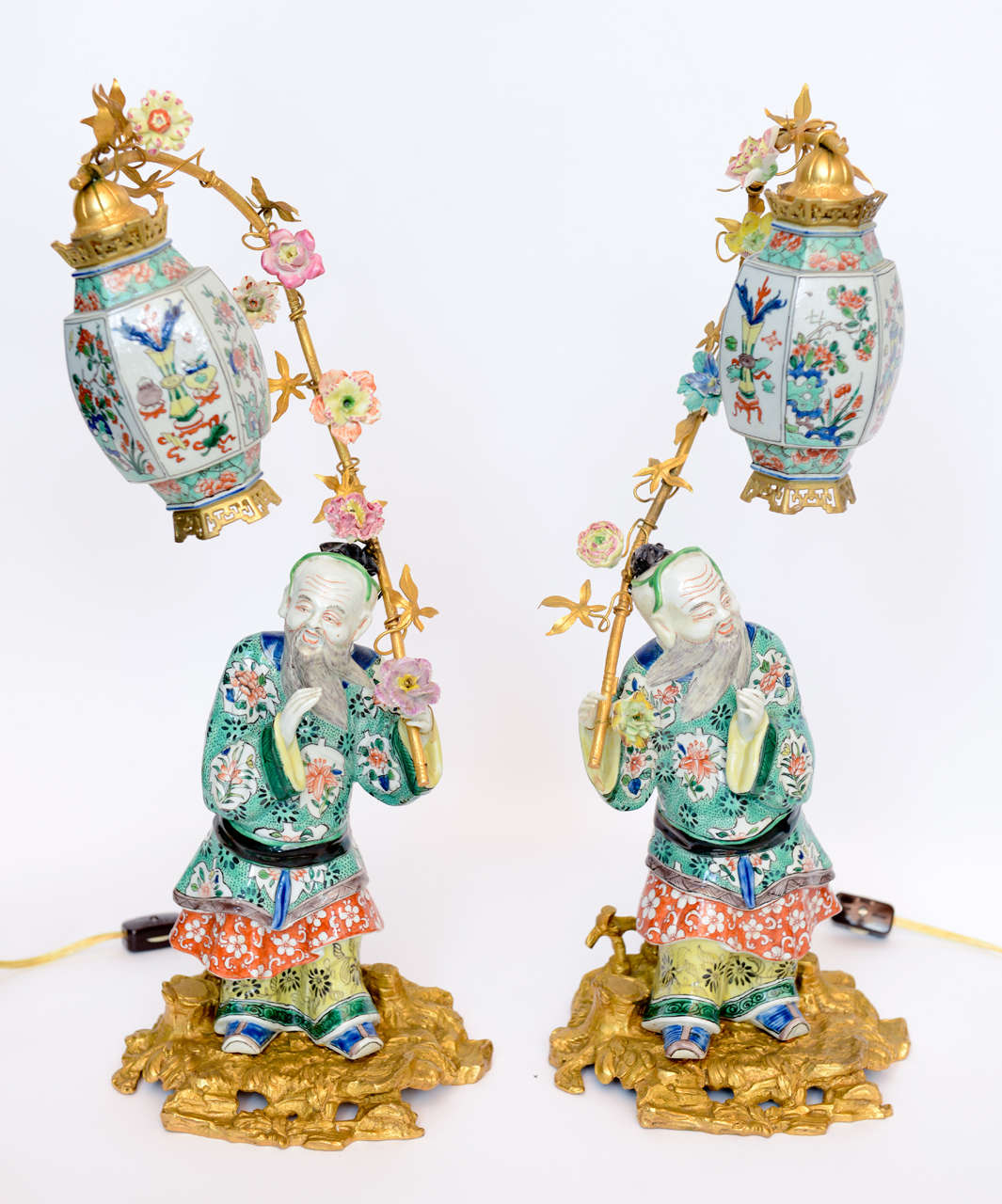 A pair of Chinese male guard figurines holding up lanterns with flowering encrusted bamboo sticks on gilt bronze bases, Circa late 19th century.