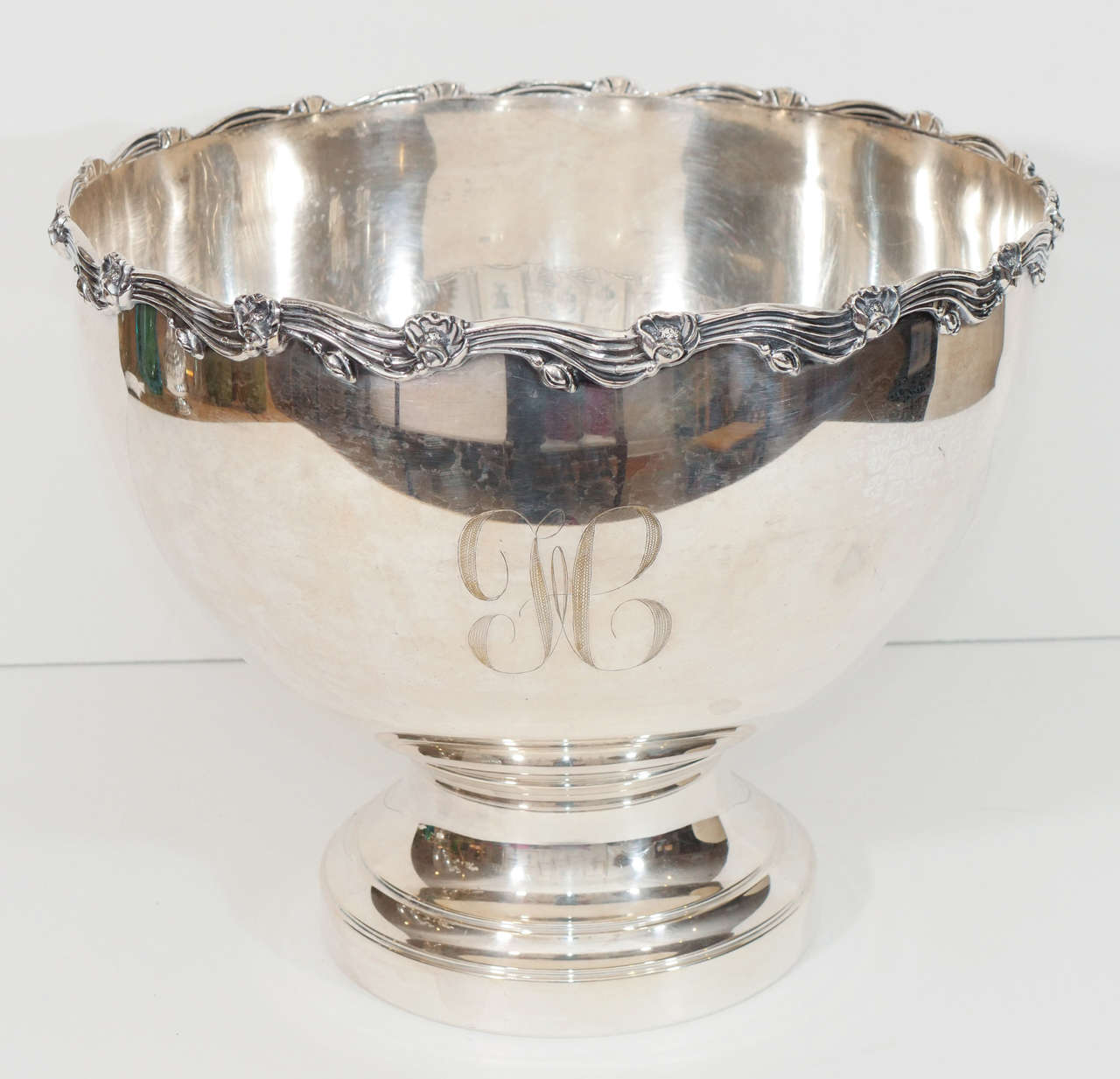 A large silverplate bowl on a round foot, with a floral design along rim. The bowl has a monogram (