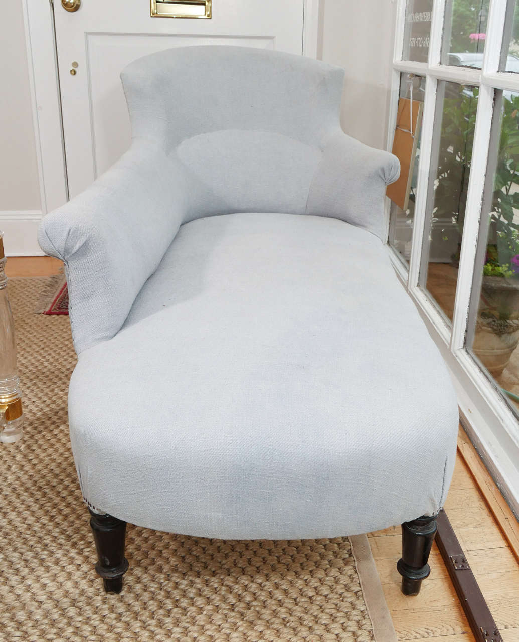 A graceful and glamorous Napoleon III chaise with turned legs on casters. This piece has a nice scale to it, and would be great either against a wall or floating in a room.  It is covered in a very pale blue/gray linen.