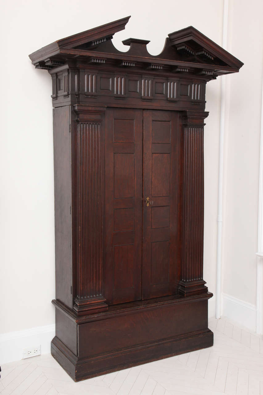 A George II stained oak cabinet of impressive architectural form with panelled doors and a concealed drawer at the base.