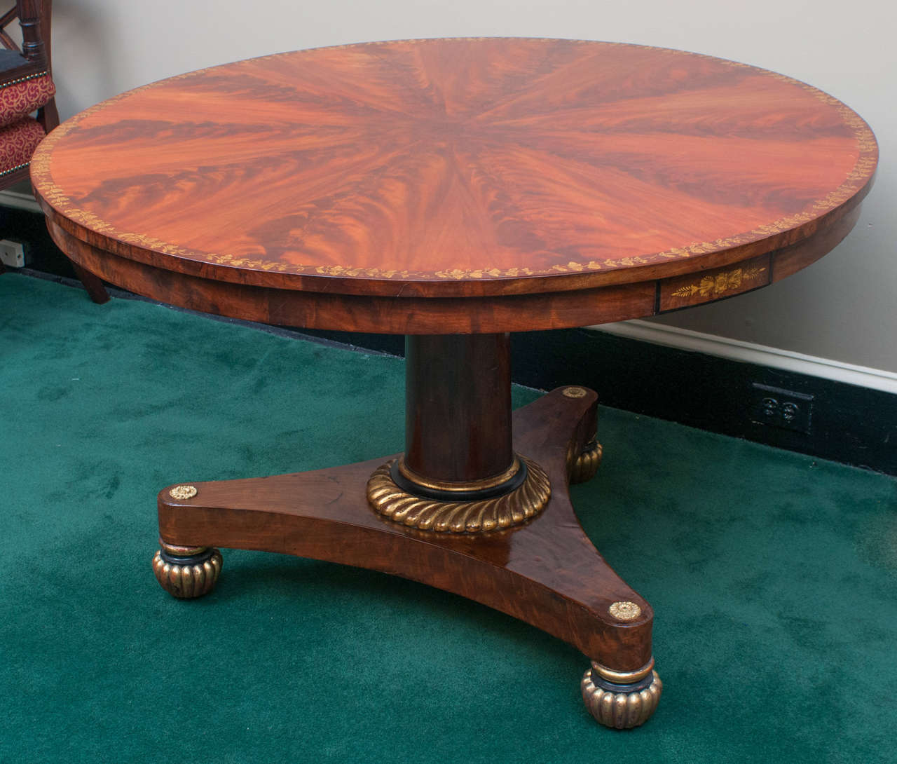 This New York table has a stunning flame mahogany veneered top laid in pie wedge sections to create a wonderful sunburst effect. Ormolu mounts adorn the base. Additional subtle decoration highlights various design elements. A gold leaf grape vine