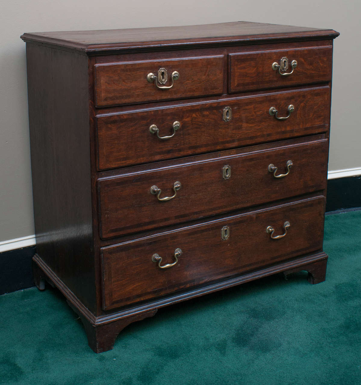 This two-over-three drawer chest has a rich, mellow patina. The banding on the top and drawer fronts, though subtle, is quite handsome.  The solid brass hardware is very old and may be original. This piece is an excellent example of a country George