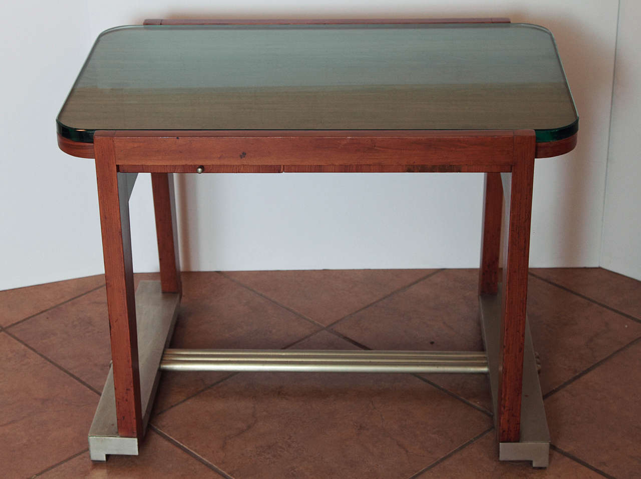 Likely a 1930s-1940s French design.
Sycamore, or the like, with brushed-plate base and stretchers, massive beveled glass top and vitrolite-lined sliding drawer.
Glass top and wooden frame canted so that glass is secured, but removable for cleaning