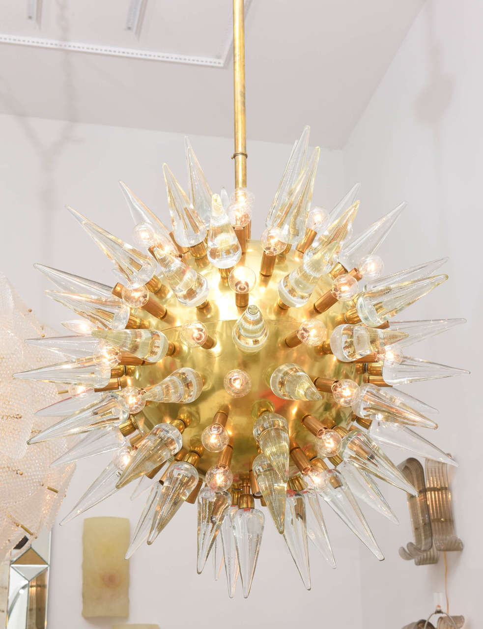Monumental Italian brass chandelier with thick clear glass spikes punctuating the brass sphere. The starburst fixture is wired and working and has multiple sockets each housing circular bulbs with candelabra sockets.