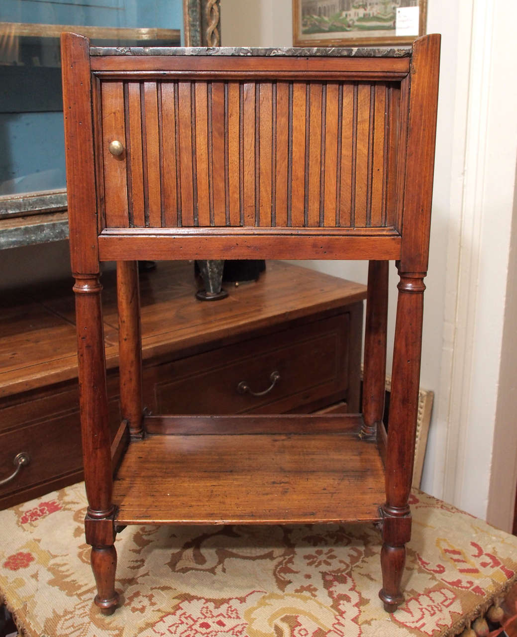A fruitwood night stand or side table with an inset marble top over a tambour door.  On turned legs supporting a shelf and over nicely carved spindle feet.  Having a simple raised edge, or gallery, and handles.