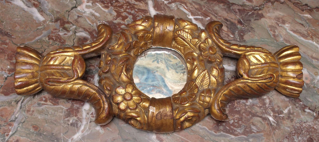 A small carved and gilded wreath with a mirror, the wreath of flowers flanked with foliate supports.  Would be nice integrated in a group of pictures or above a painting or doorway.