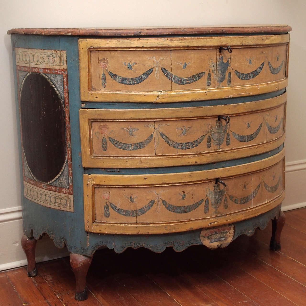 A very special piece: a rare Italian polychrome commode, in demilune shape, having three drawers over a scalloped apron and on cabriole legs.  The drawers decorated with urns and garland swags suspended by ribbons and faces and punctuated with