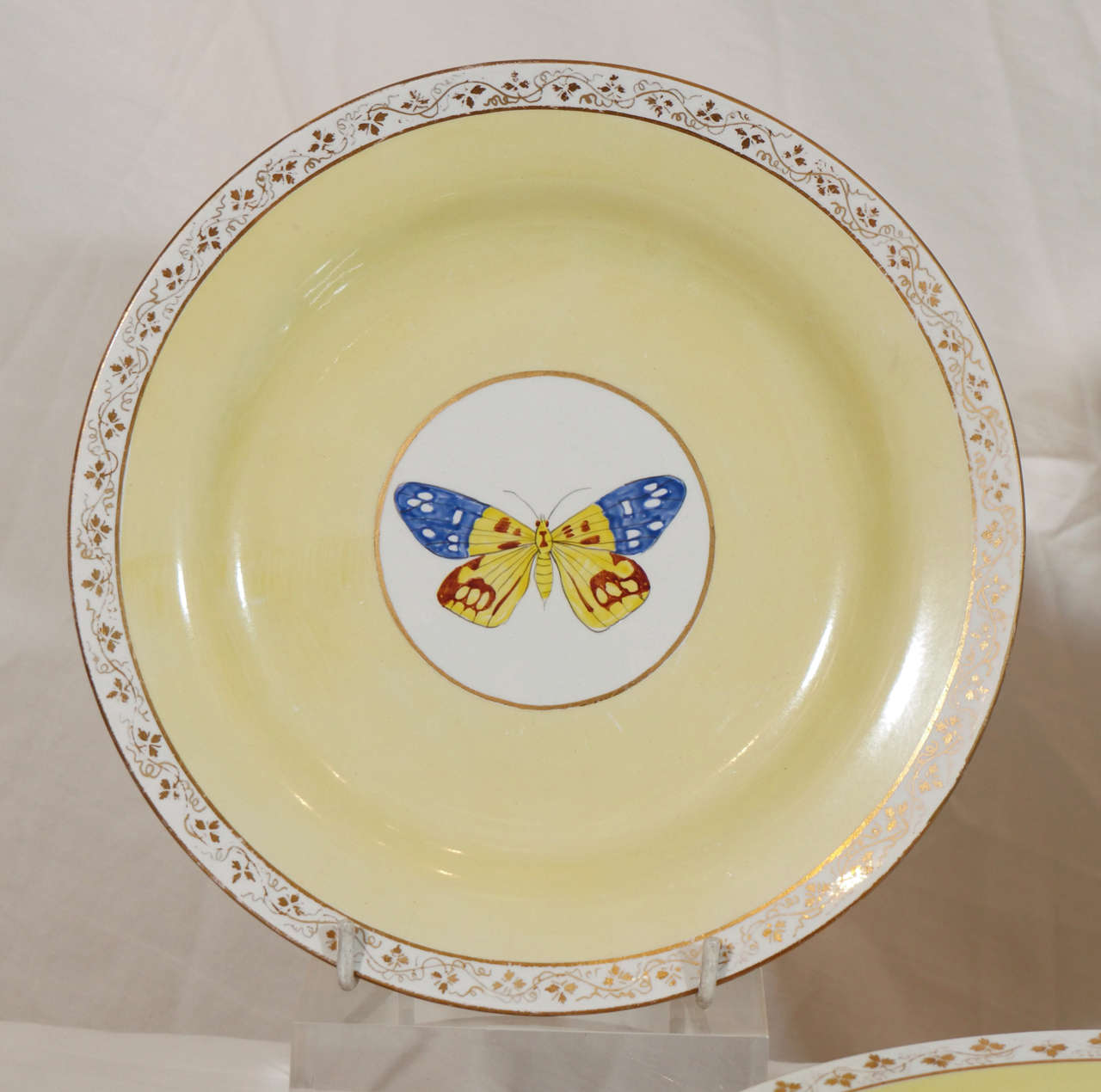 A group of decorative pottery plates each with a hand painted image of a single butterfly reserved at the center and surrounded by an elegant yellow ground.The plates are impressed Wedgwood.