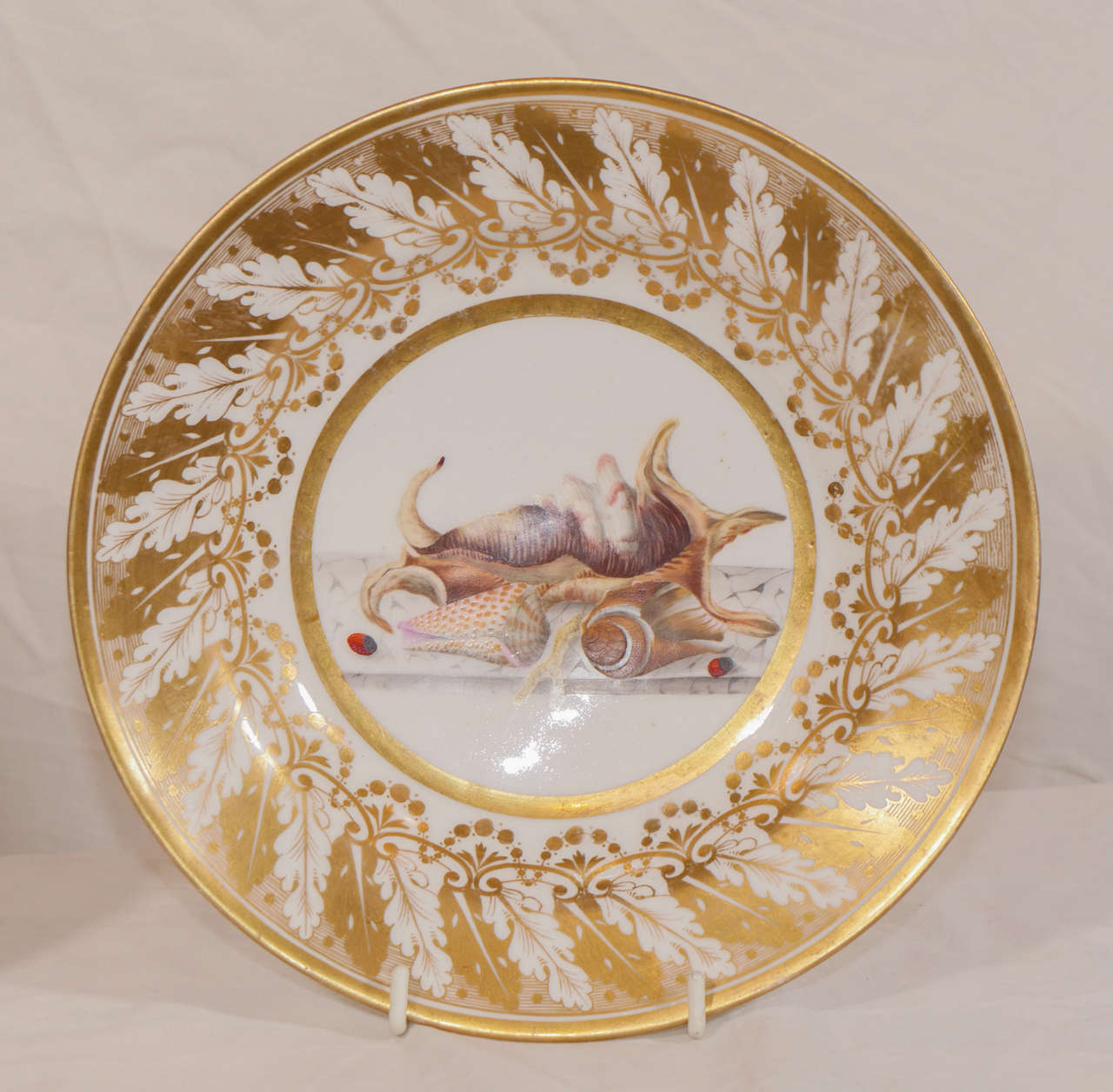 Both dishes decorated to the center with well painted shells. The broad borders beautifully gilded with acanthus leaves. In the early part of the 19th century Derby was well known for dishes with this type of broad gilded border worked around