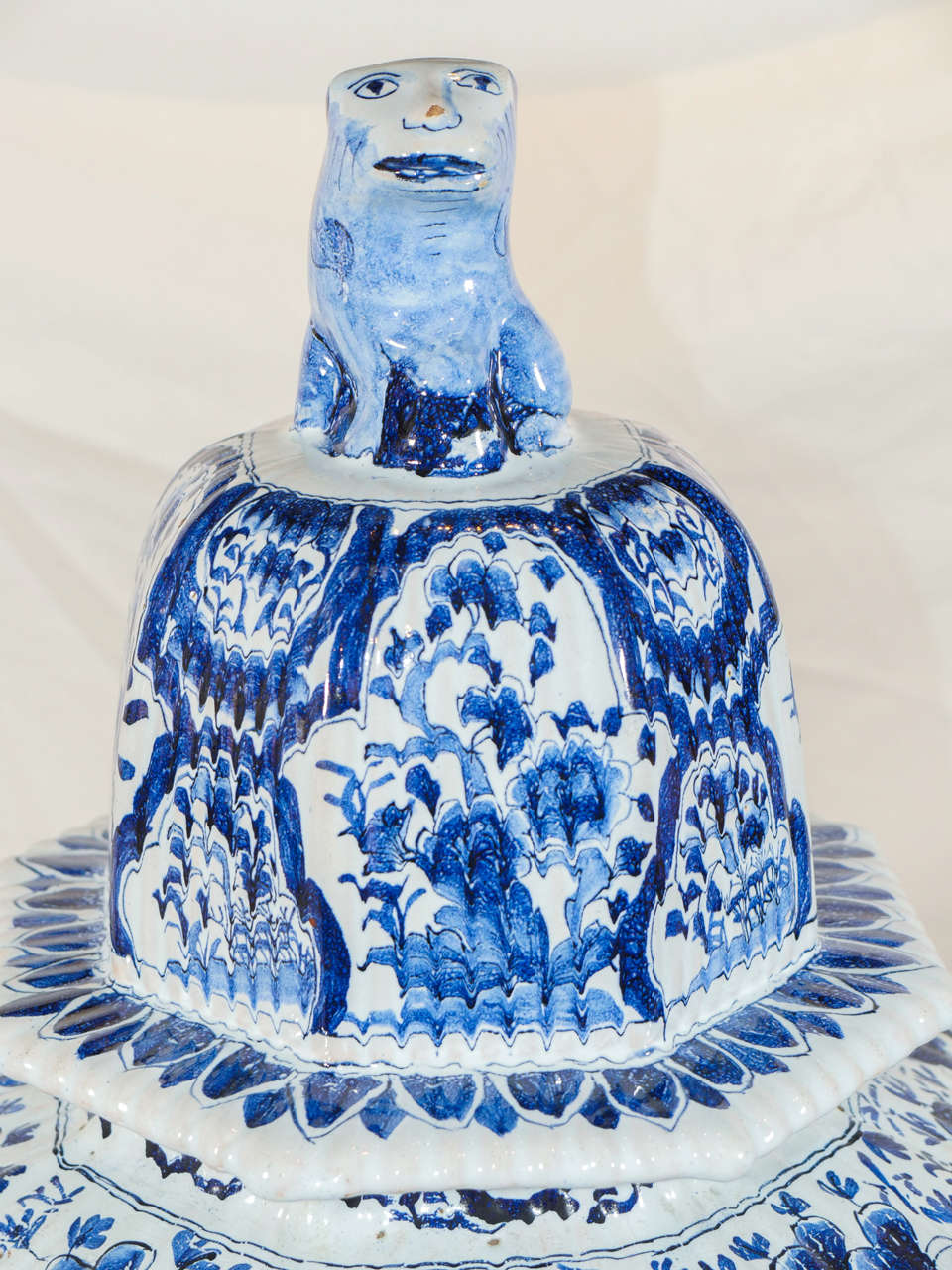 A Dutch Delft blue and white octagonal covered vase: fluted with panels showing a song bird in flight over a flower filled garden. The cover is similarly decorated with flowers, and has a traditional lion form finial.