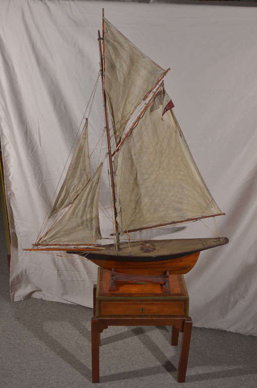 Large antique wood pond yacht on stand with 2 flags over the name  Sappho on the deck. The sails have red stitching which was done on a treadle sewing machine.