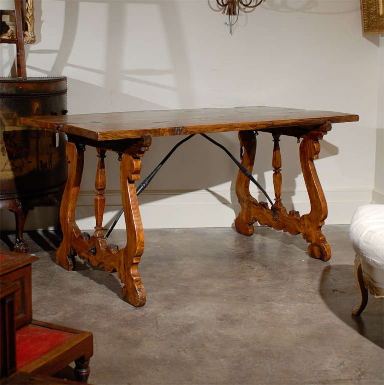 A 19th century long Italian wooden trestle table featuring a rectangular two-planked top with beautiful wood grain and knots. The table sits on two flattened lyre-shaped legs with a central baluster. Two iron stretchers join together the supports,