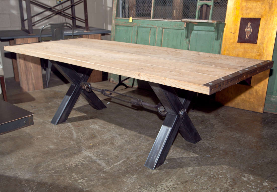 Industrial style steel base dining table, the base with a steel X-frame joined by a ratchet spring stretcher, and the top made of reclaimed pine planks with steel cleated ends. A fantastic dining table.