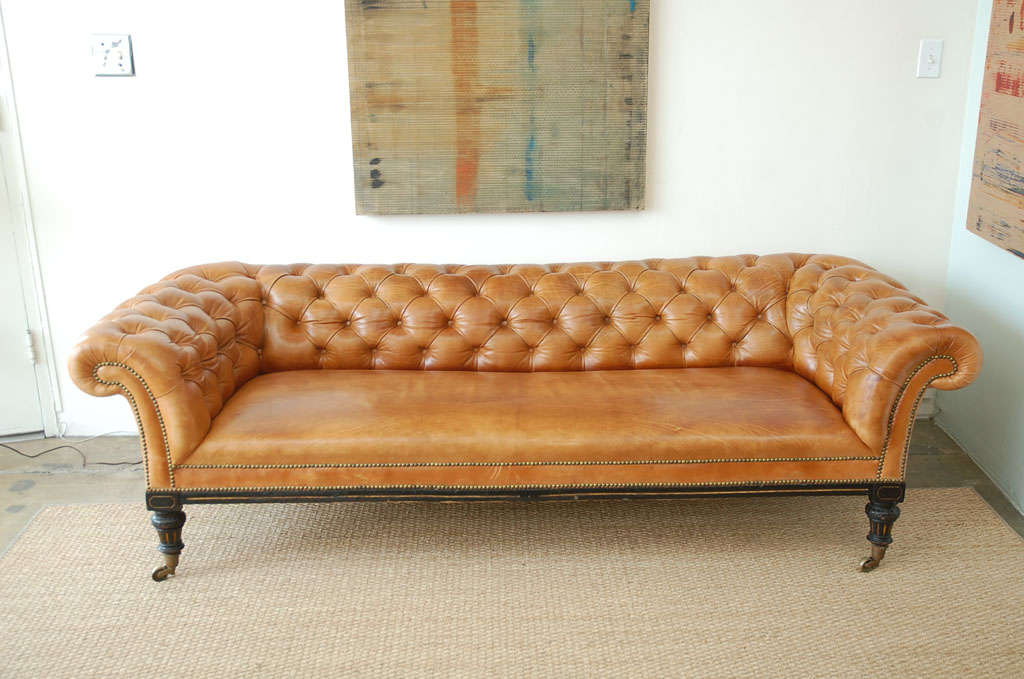 Not your typical Chesterfield, this design is low, contemporary and sleek. Upholstered in sumptuous caramel tufted leather with black paint-finish wood legs and trim with gold detailing. Brass casters and nail heads accent the front.