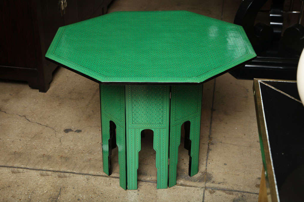 A green lacquered octagonal table from Thailand with removable top and folding base, all decoratively trimmed in a black and gold traditional pattern