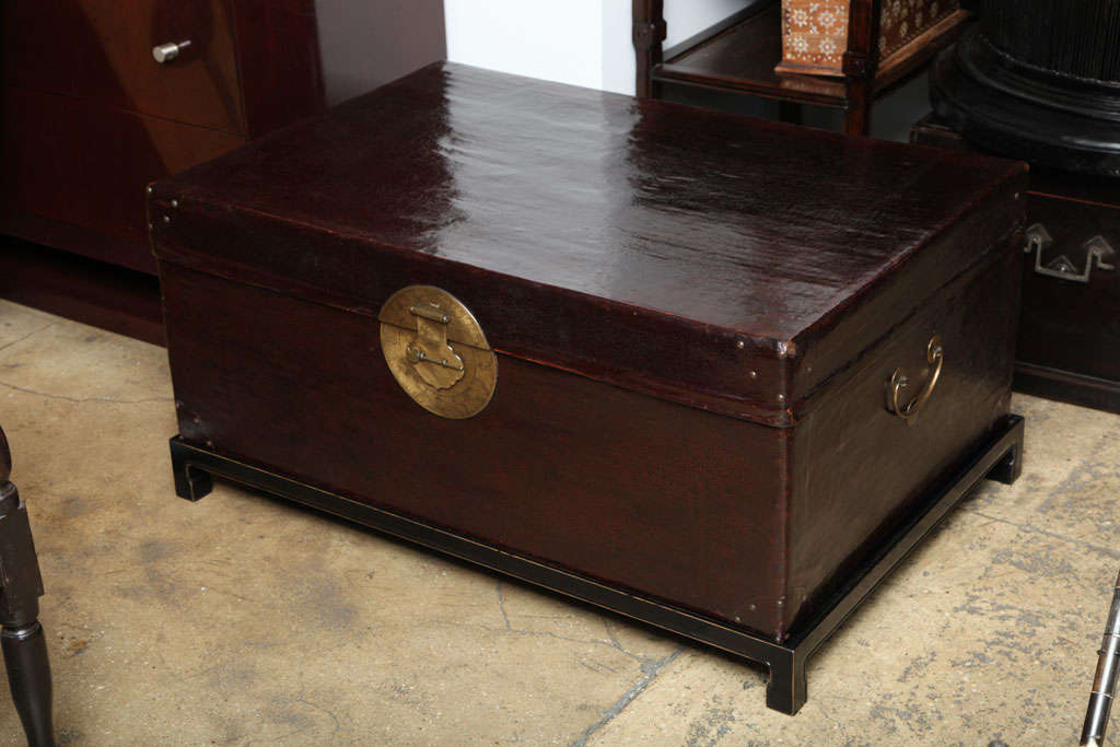 A dark leather trunk from China with tradtional brass fixtures on a black wood base