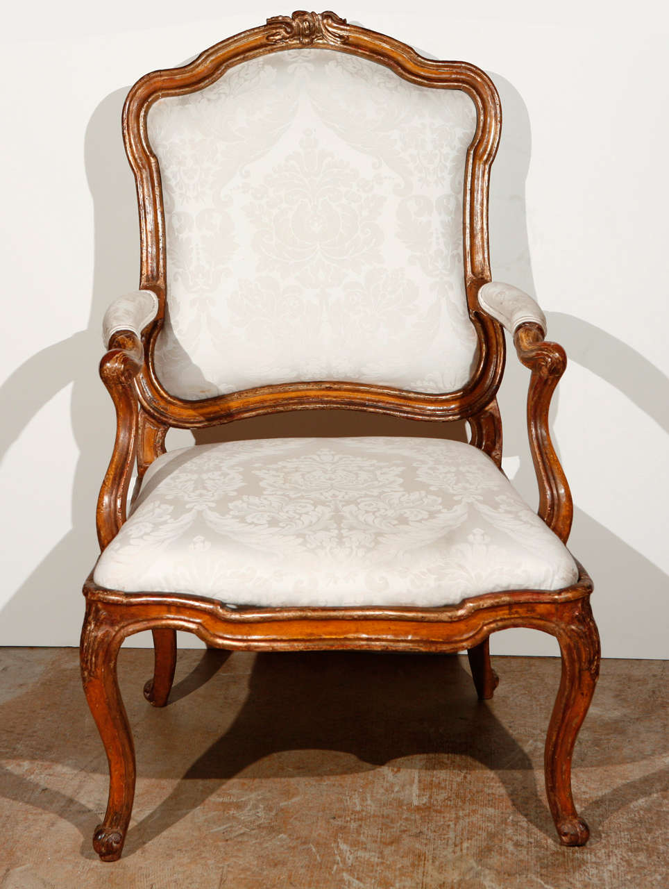Hand-carved and gilded, Italian, open-arm, Rococo-style armchair with cabriole legs and elegant, serpentine arms. Top rail boasts a foliate relief carving. 