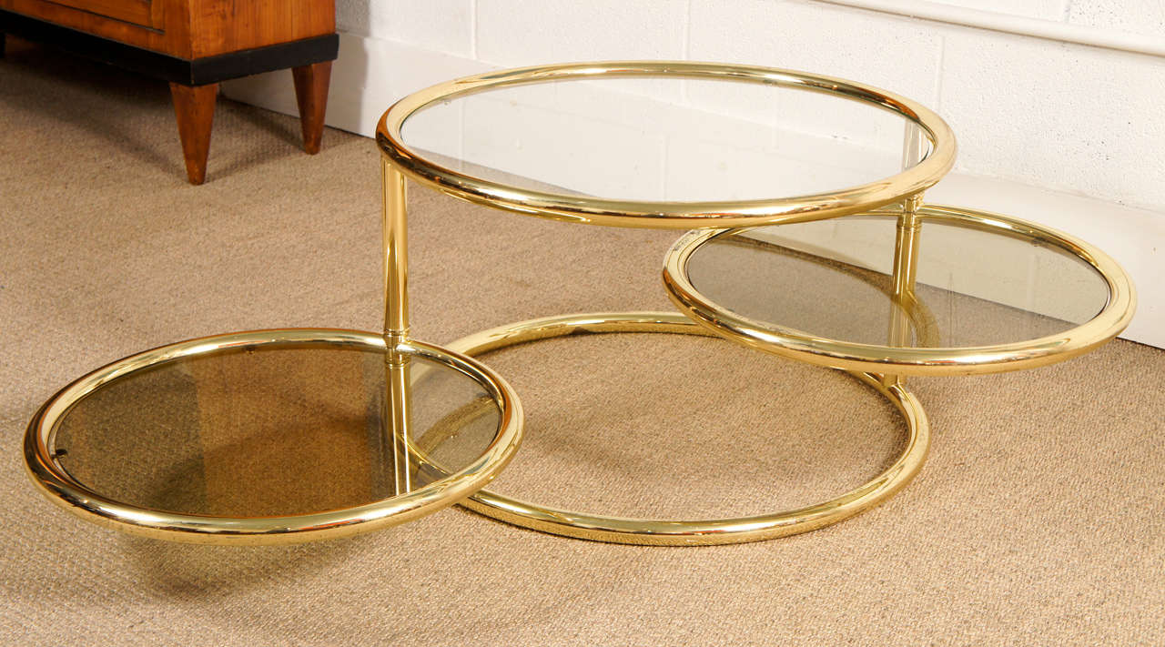Here is a brass three ring table with swivel tops and great style. 
The top is stationary while the two rings have full swing. The top has clear glass and the two smaller tops are smoked.