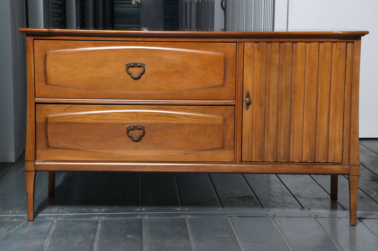 A Mid-Century Heywood Wakefield credenza with two drawers. Drawers feature original brass hardware. Cabinet door has a raised articulating ribbon pattern. Cabinet interior has one fixed shelf. Heywood Wakefield stamp inside top drawer. Original