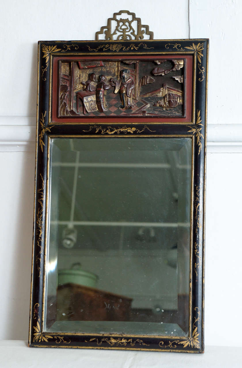 19th century ebonized Chinese mirror with carved cartouche
of figures inside a red border. Gold details on the border. Beveled mirror. Brass hanging detail.