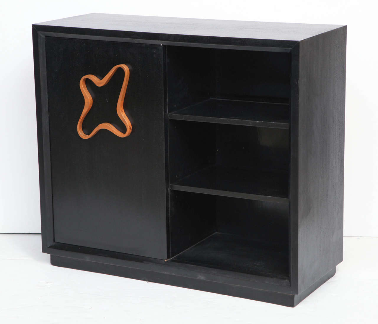 A pair of satin-black painted mahogany cabinets with bold quatrefoil pulls in light fruitwood. The cabinets are designed as a matching left/right pair, each having one open side with two adjustable shelves and a center-hinged door revealing two