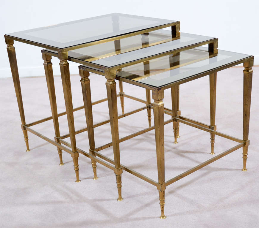 A set of three Maison Jansen nesting tables with solid brass frames and smokey glass tops.