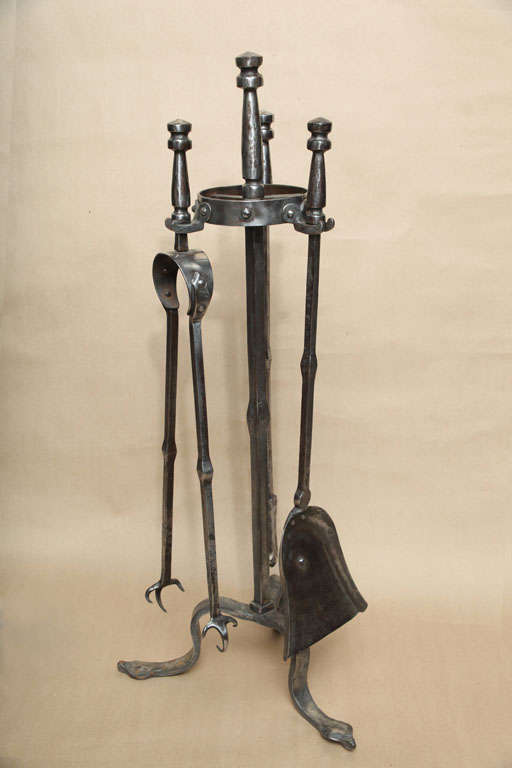 Fine set of English Cotswold School wrought iron firetools, comprising a solid shovel, poker and talon ended tongs, with original stand with pointed penny feet.