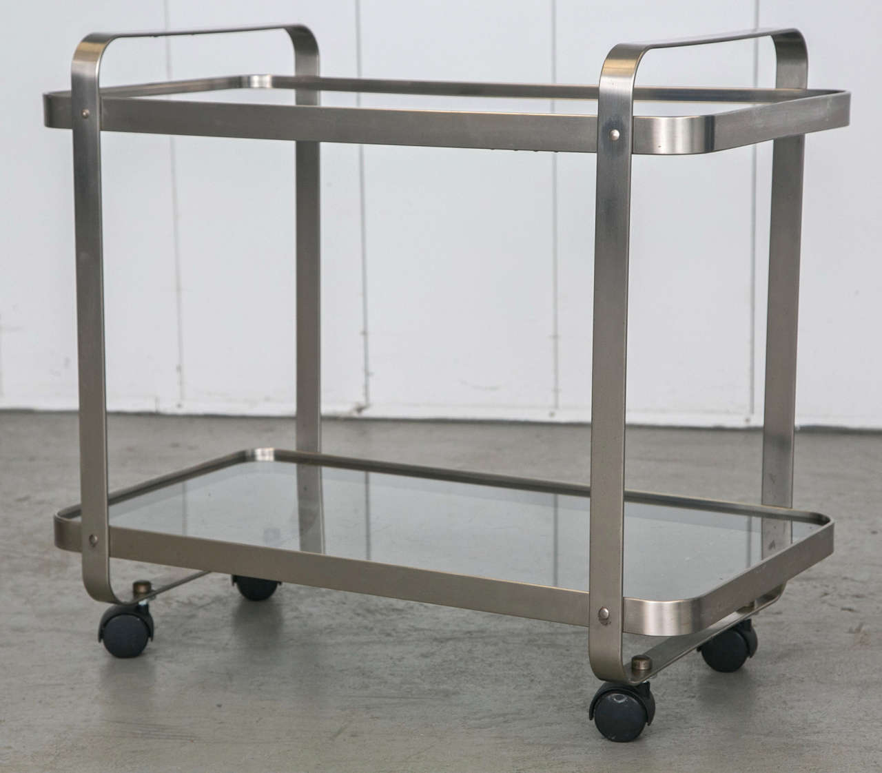 A streamlined modern steel rectangular rolling cart with glass shelves