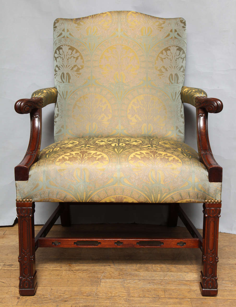 An English mahogany Chinese Chippendale style open arm chair. The upholstered back with arched top flanked by upholstered arms with up swept mahogany supports having scroll shaped hand rests. The square legs with closed fret Neo-Gothic tracery