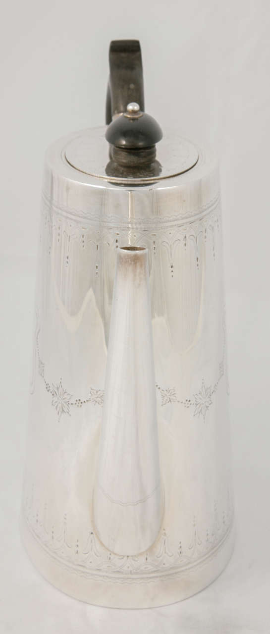 Silver plate coffee pot, circa 1880. Dainty detail on the body of the coffee pot, with a dark wooden handle and lid.
