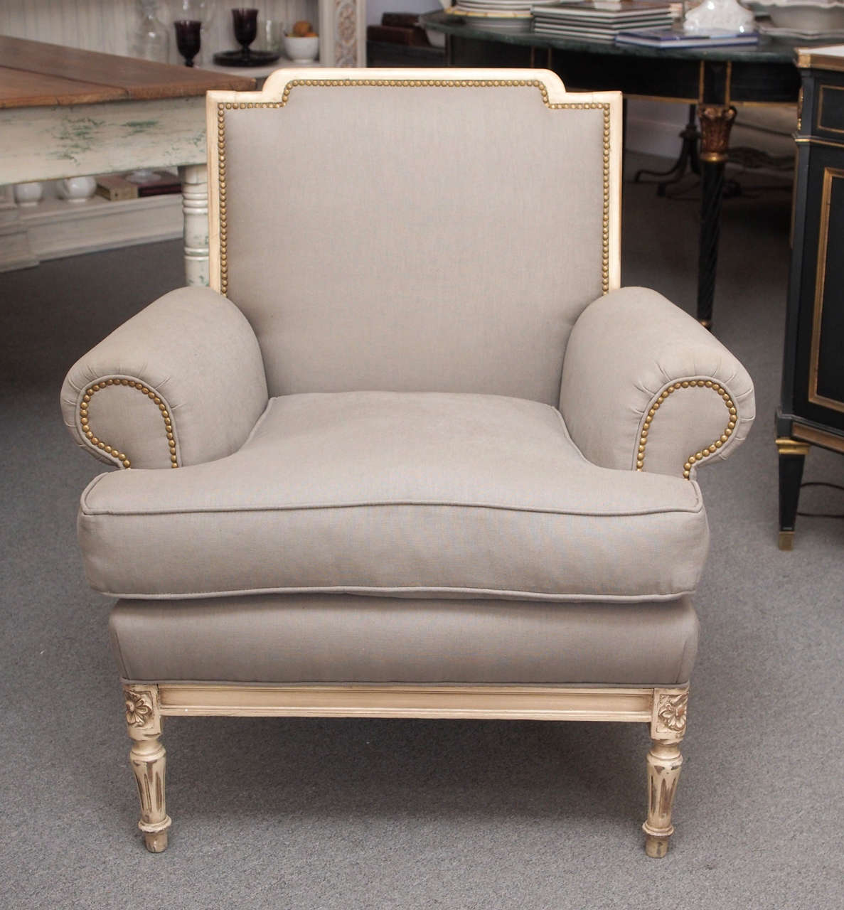 Pair of armchairs with rolled arms and a removable seat cushion, upholstered in gray fabric with nailheads. Fluted legs ending in toupie feet support the cream color painted wood frame having rails ornamented with floral carved corner blocks,
