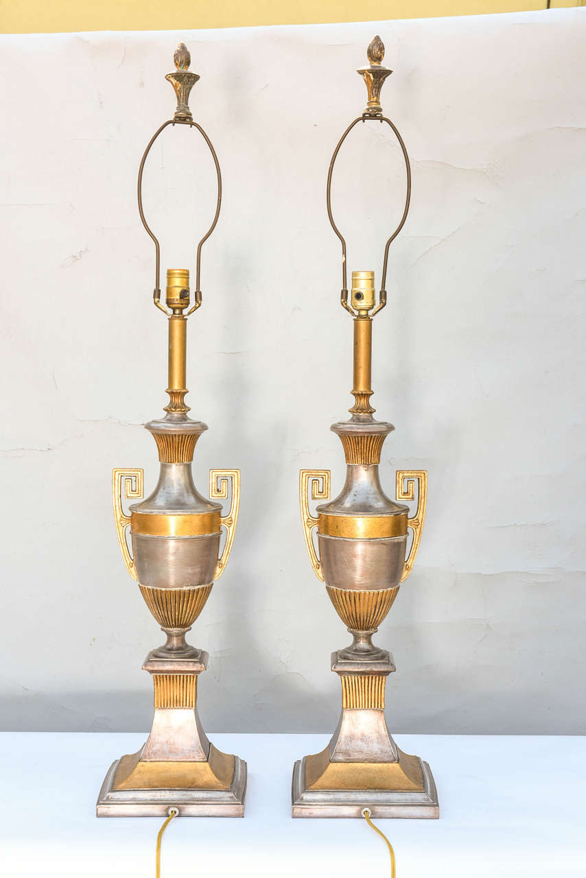 Pair of contemporary neoclassical lamps, of polished spelter with gilded accents, each amphora form urn with handles ending in Greek Key motif, raised on concave graduated plinth.

Measured to top of finial (with #10 harp) 42.25